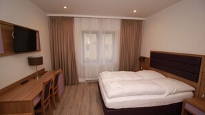 Habitación de hotel con cama, escritorio, silla, televisor y ventana con cortinas.