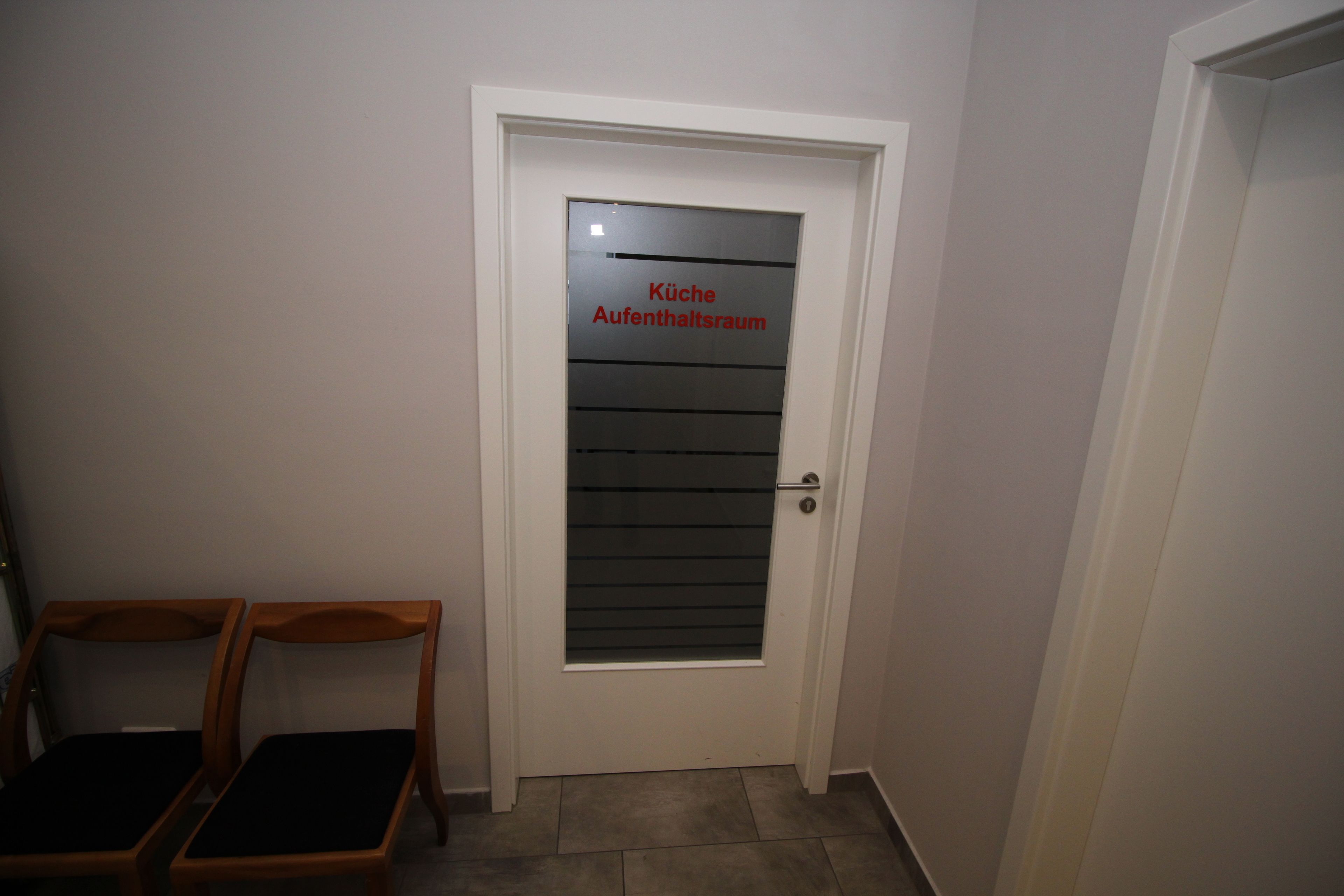 Una puerta con un panel de vidrio esmerilado y un letrero que dice 'Küche Aufenthaltsraum'.