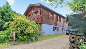 Un chalet en bois doté d’un balcon, entouré de verdure et bordé d’un chemin de gravier.