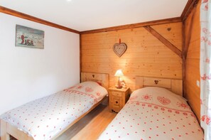 A bedroom with two single beds, wooden headboards, a nightstand with a lamp, and a heart-shaped decoration on the wall. - Homerez - Chalet in Stosswihr (Stosswihr)