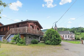 A traditional wooden house with a balcony, a stone lower level, and a church in the background. - Homerez - Chalet in Stosswihr (Stosswihr)