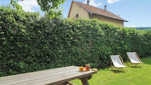 Une table de pique-nique en bois, avec deux chaises et un banc, un pot de confiture et une bougie posés sur la table.