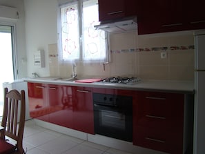 A kitchen with red cabinets, a gas stove, a sink, and a window with floral curtains.