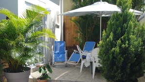 A patio with two blue lounge chairs, a white umbrella, and potted plants. - Maisonnette with mezzanine, air conditioning, secure parking, wifi internet, Rated 3 stars. (st pierre)