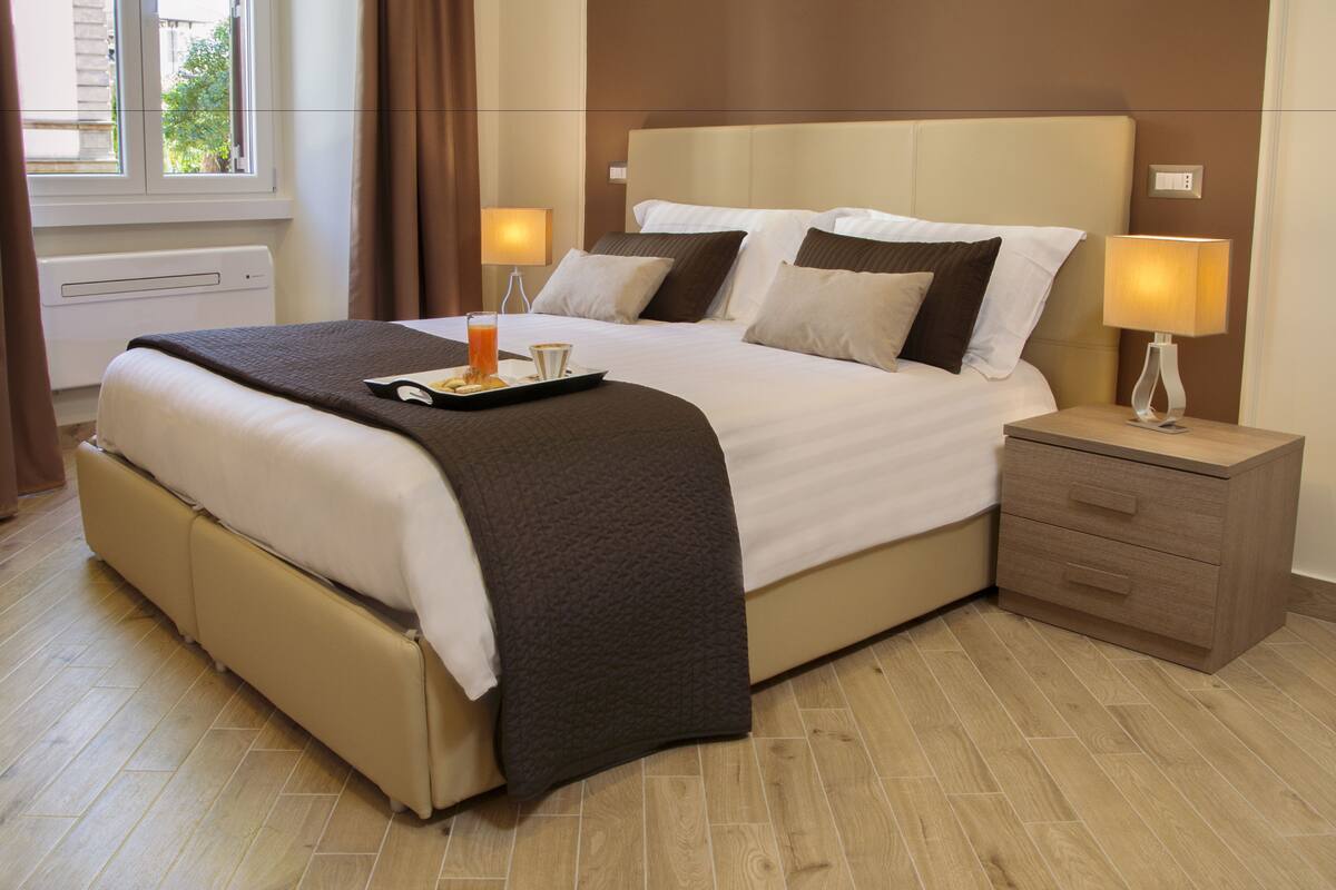 A hotel room with a large bed, bedside lamps, a tray with breakfast, and a window with curtains.