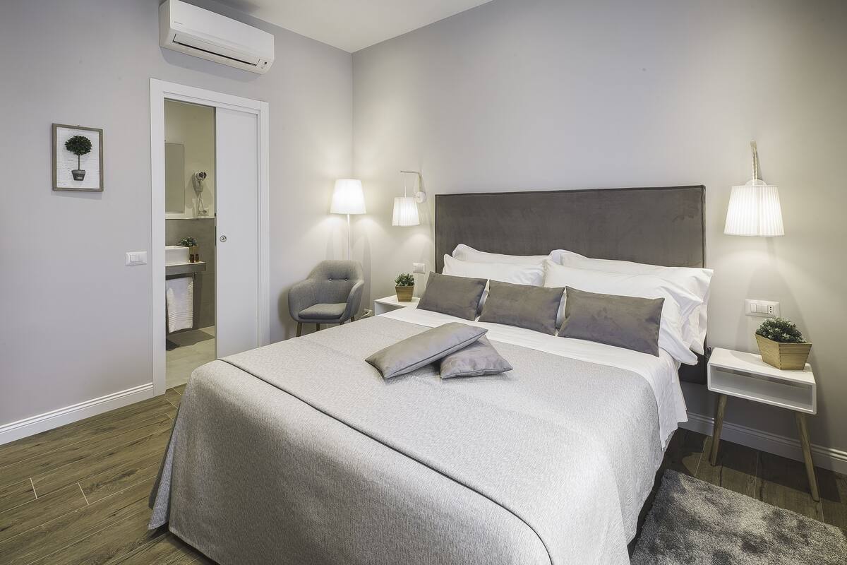 A bedroom with a bed, bedside tables, a chair, and an air conditioning unit.