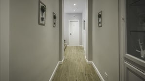 Un pasillo estrecho con suelo de madera, paredes blancas y cuadros enmarcados.