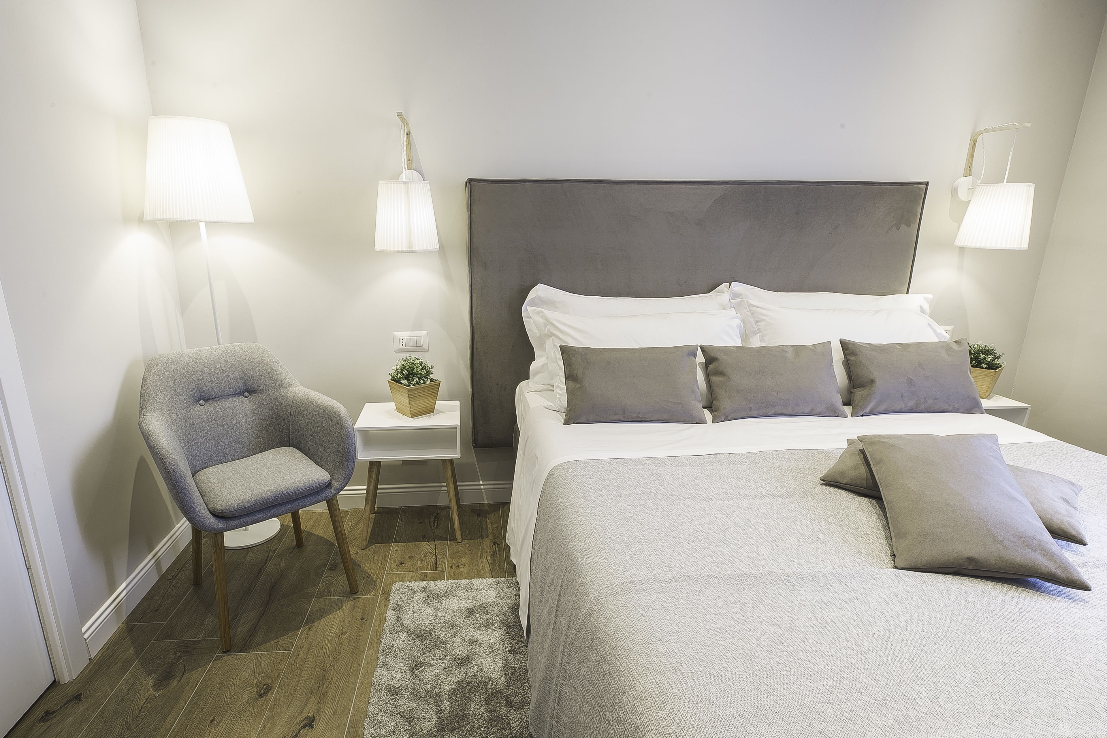 Une chambre bien rangée, avec un lit, une chaise, des tables de chevet et des lampes fixées au mur.