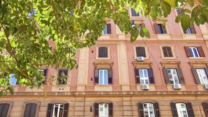 Un edificio de varios pisos con un estilo arquitectónico clásico, que presenta ventanas uniformemente espaciadas con contraventanas, una entrada central con arco y un balcón en el piso superior.