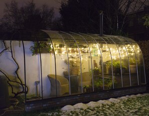 Uma estufa com telhado curvo, iluminação interna e plantas em vasos.