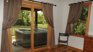 Una habitación con una puerta corrediza de vidrio que da a un área con jacuzzi exterior, una silla de madera y un aparador de madera.