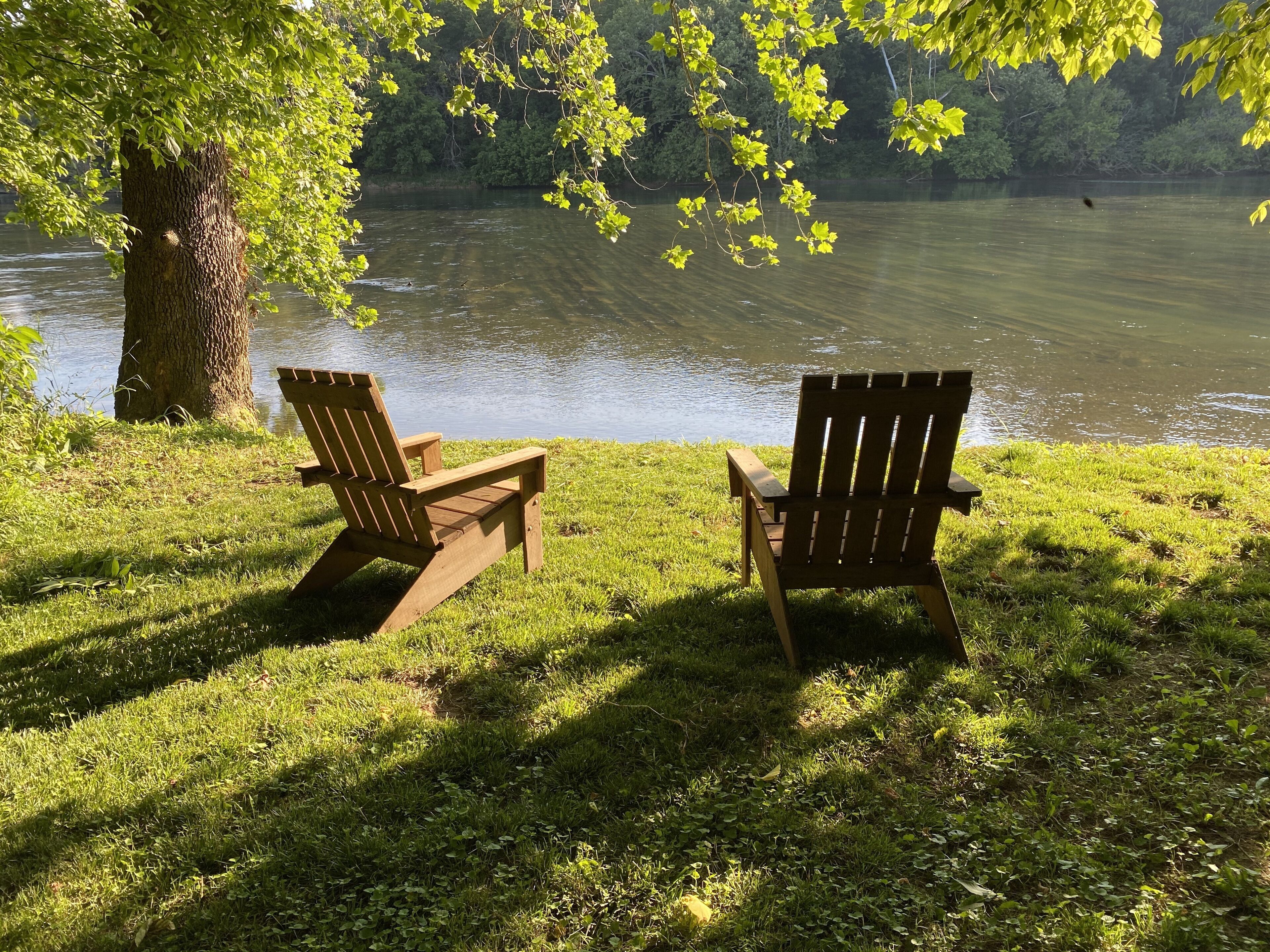 Duas cadeiras Adirondack viradas para um lago, com uma árvore ao primeiro plano.
