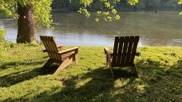 Duas cadeiras Adirondack viradas para um lago, com uma árvore ao primeiro plano.