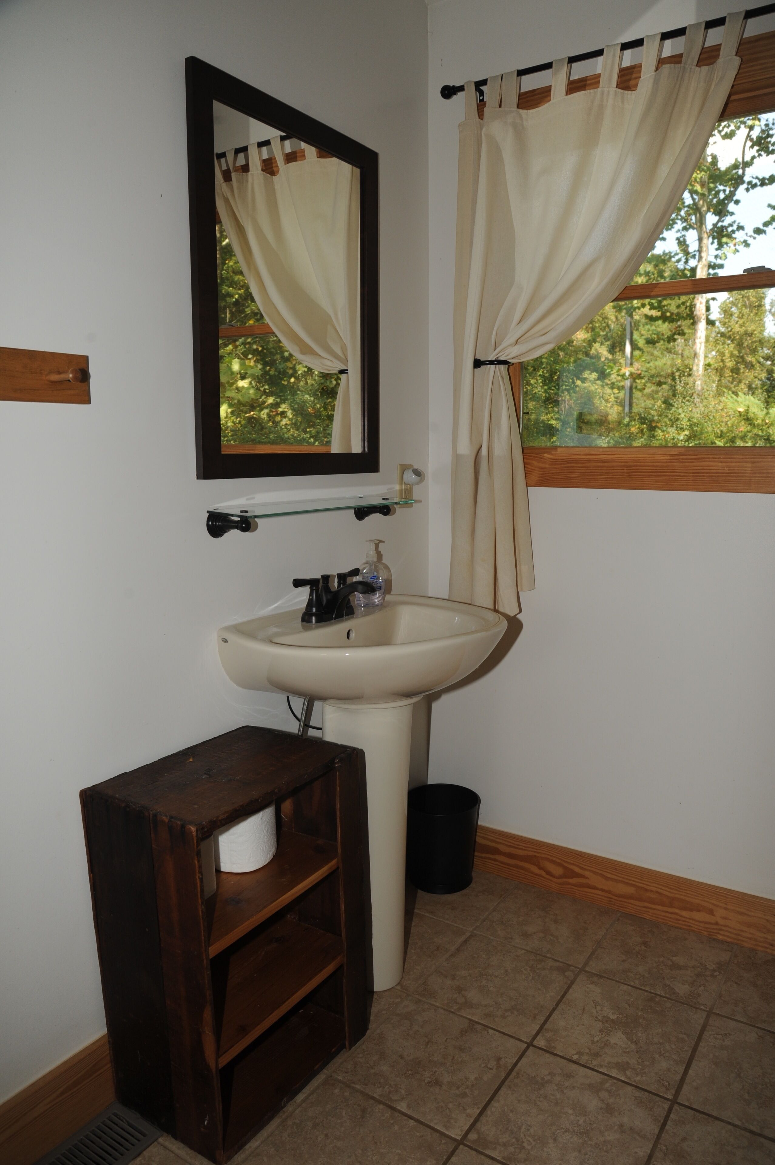 Un baño con lavamanos, espejo y ventana con cortinas.