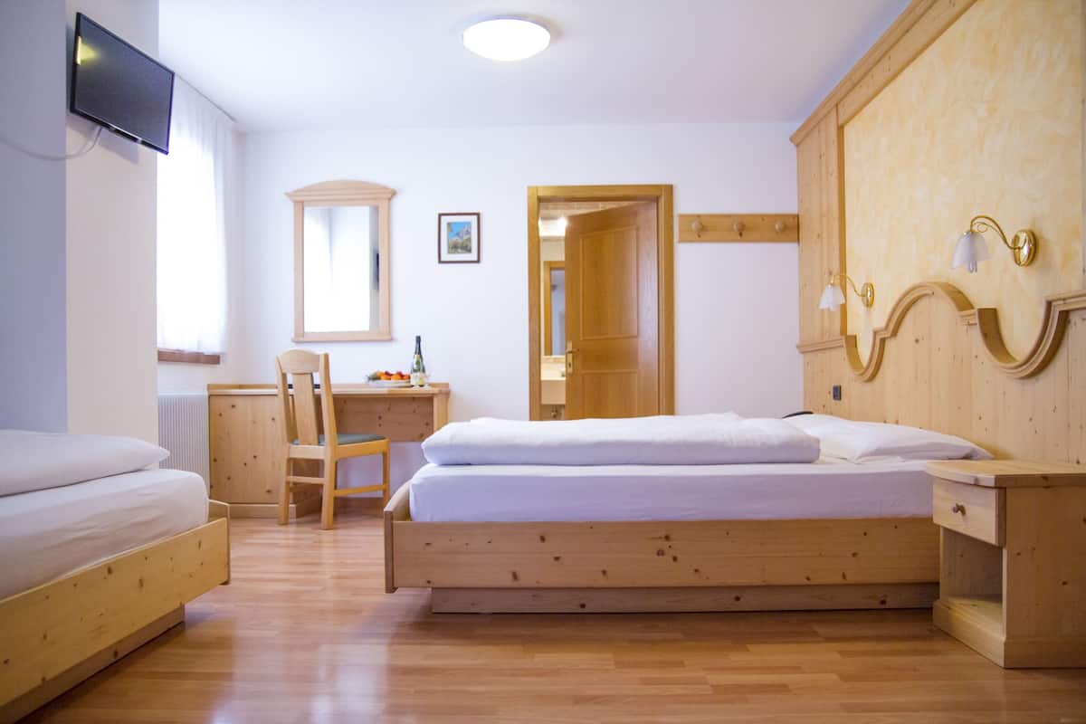 A bedroom with a wooden bed, a desk, a chair, a television, and a mirror.