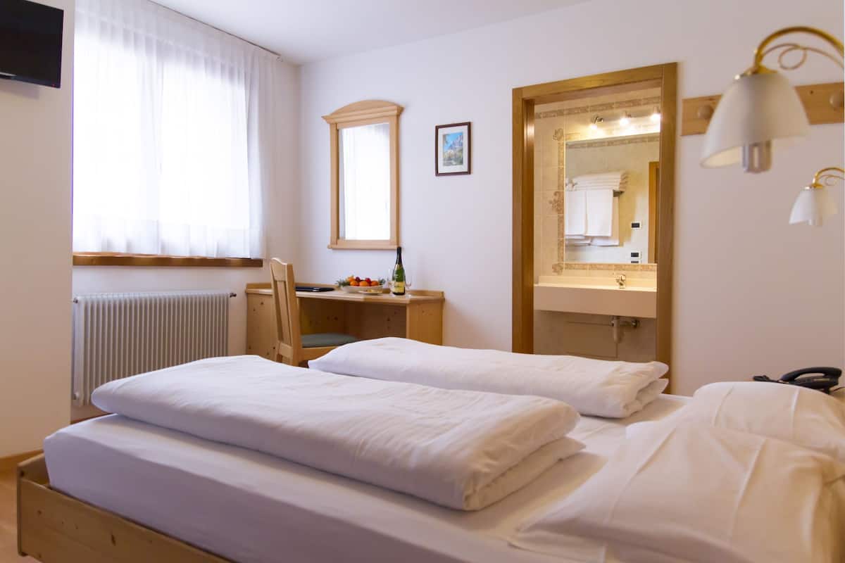 A hotel room with two beds, a desk with a chair, a large mirror, and a radiator.