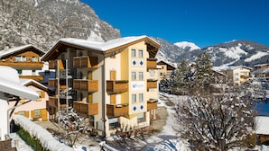 A multi-story hotel with balconies, a snow-covered landscape, and mountains in the background.