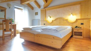 A wooden-framed bedroom with a bed, bedside lamps, a chair, and a small bedside table.