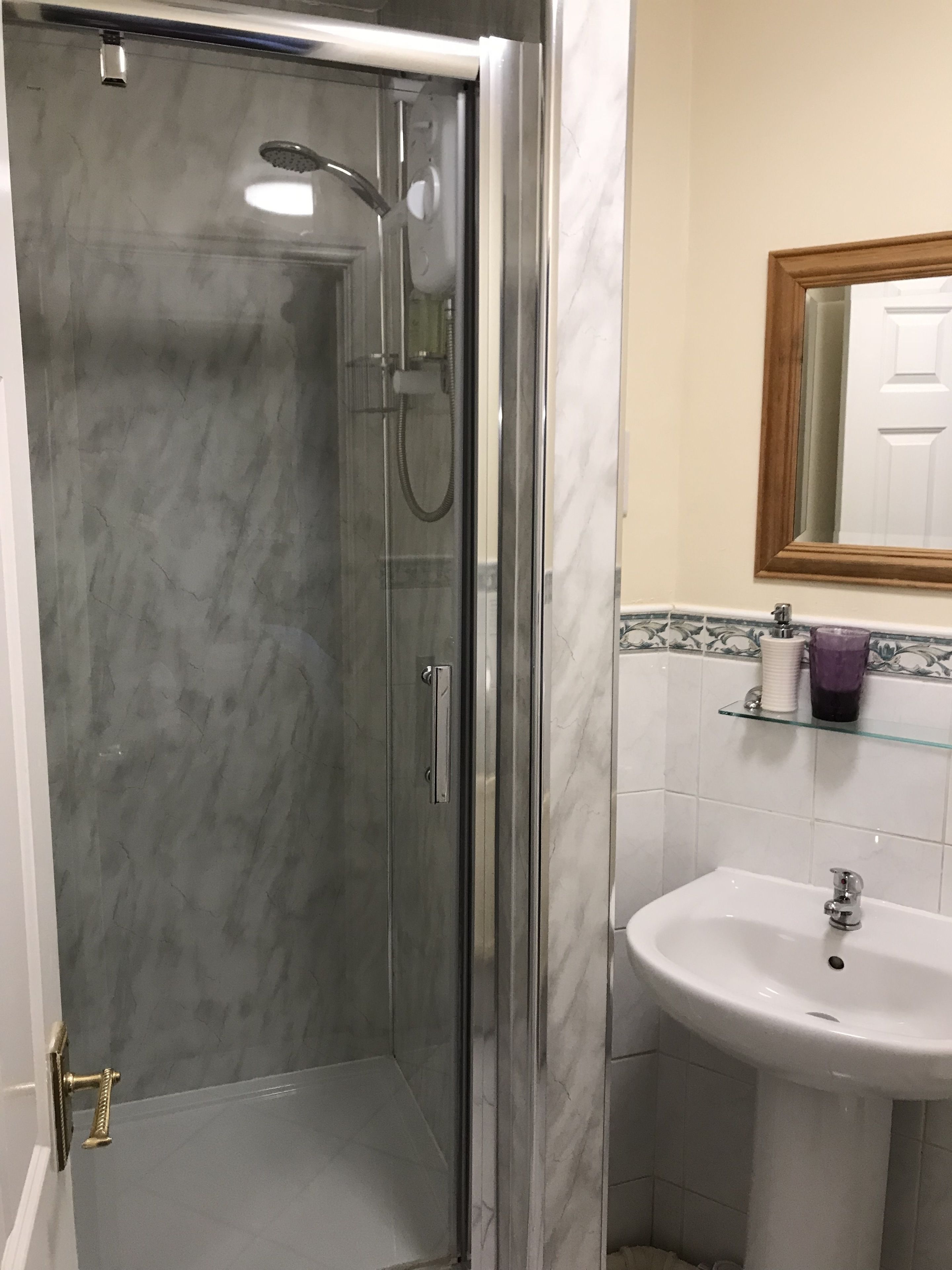 A bathroom with a glass-enclosed shower, a white sink, and a mirror above it.