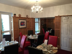 A dining area with wooden paneling, red chairs, a chandelier, and framed artwork on the walls. - Clayhanger Guest House (Newcastle-Under-Lyme)