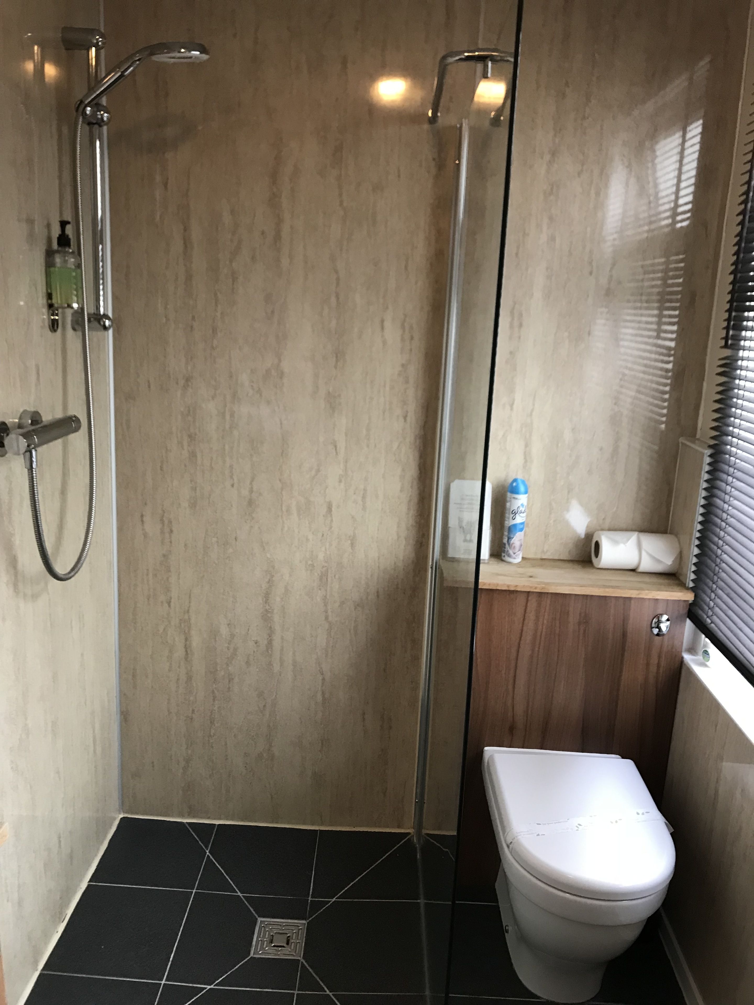 Un baño moderno con ducha de vidrio, inodoro y estante con artículos de aseo.