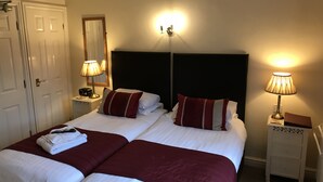 A double bed with two pillows, a bedside table with a lamp, a nightstand with a lamp, and a door.