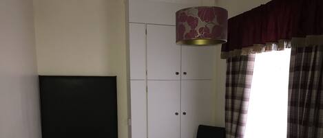 A hotel room with a bed, a chair, a wardrobe, and a window with curtains.