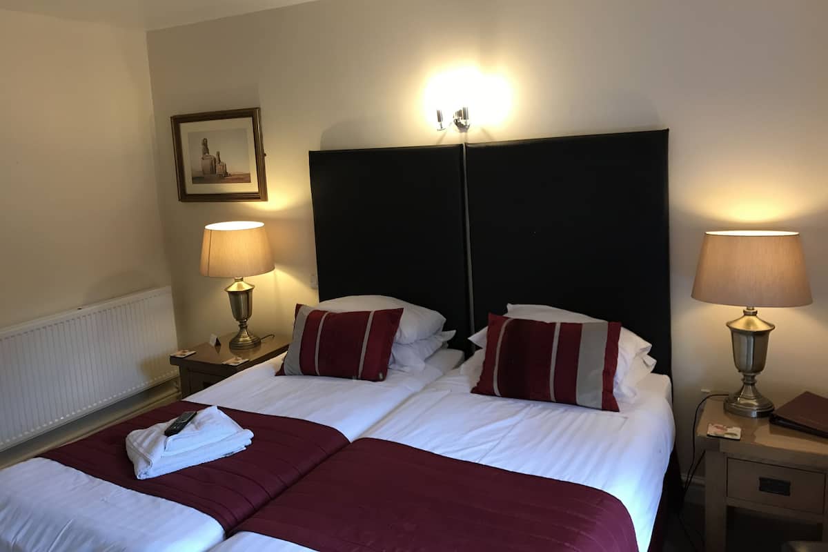 Une chambre d’hôtel avec deux lits, chacun agrémenté d’un oreiller à rayures rouges et blanches, et une table de chevet avec une lampe.
