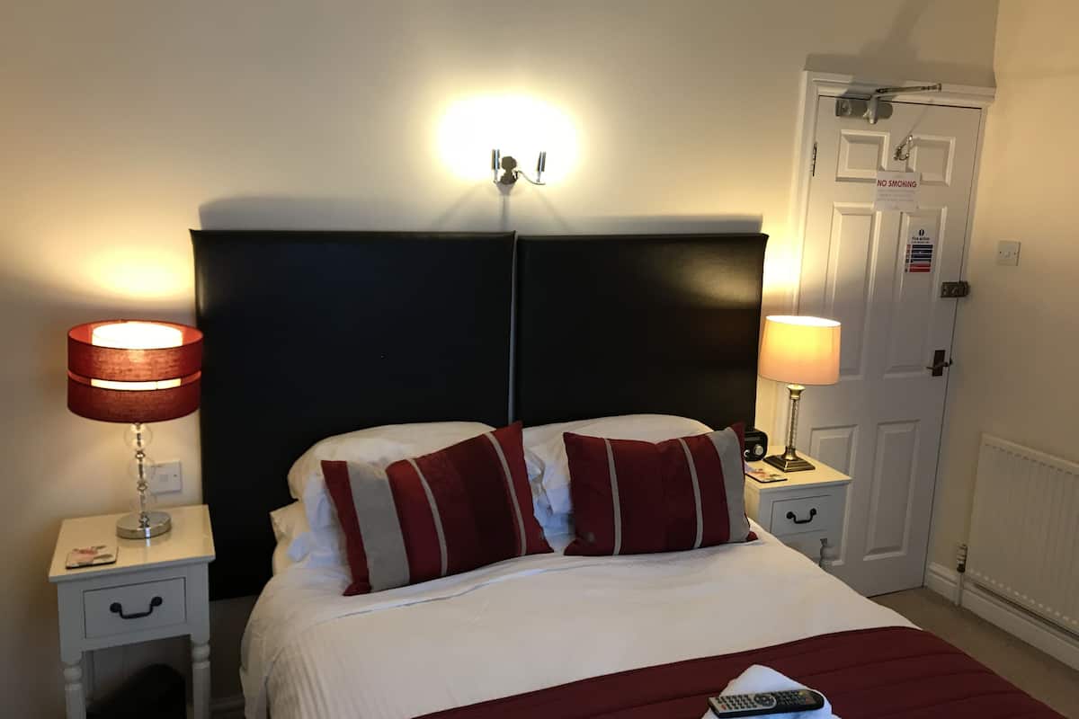 Une chambre d’hôtel comprenant un lit, deux lampes de chevet, une table de chevet, une porte avec un panneau « Interdiction de fumer » et un luminaire fixé au mur.