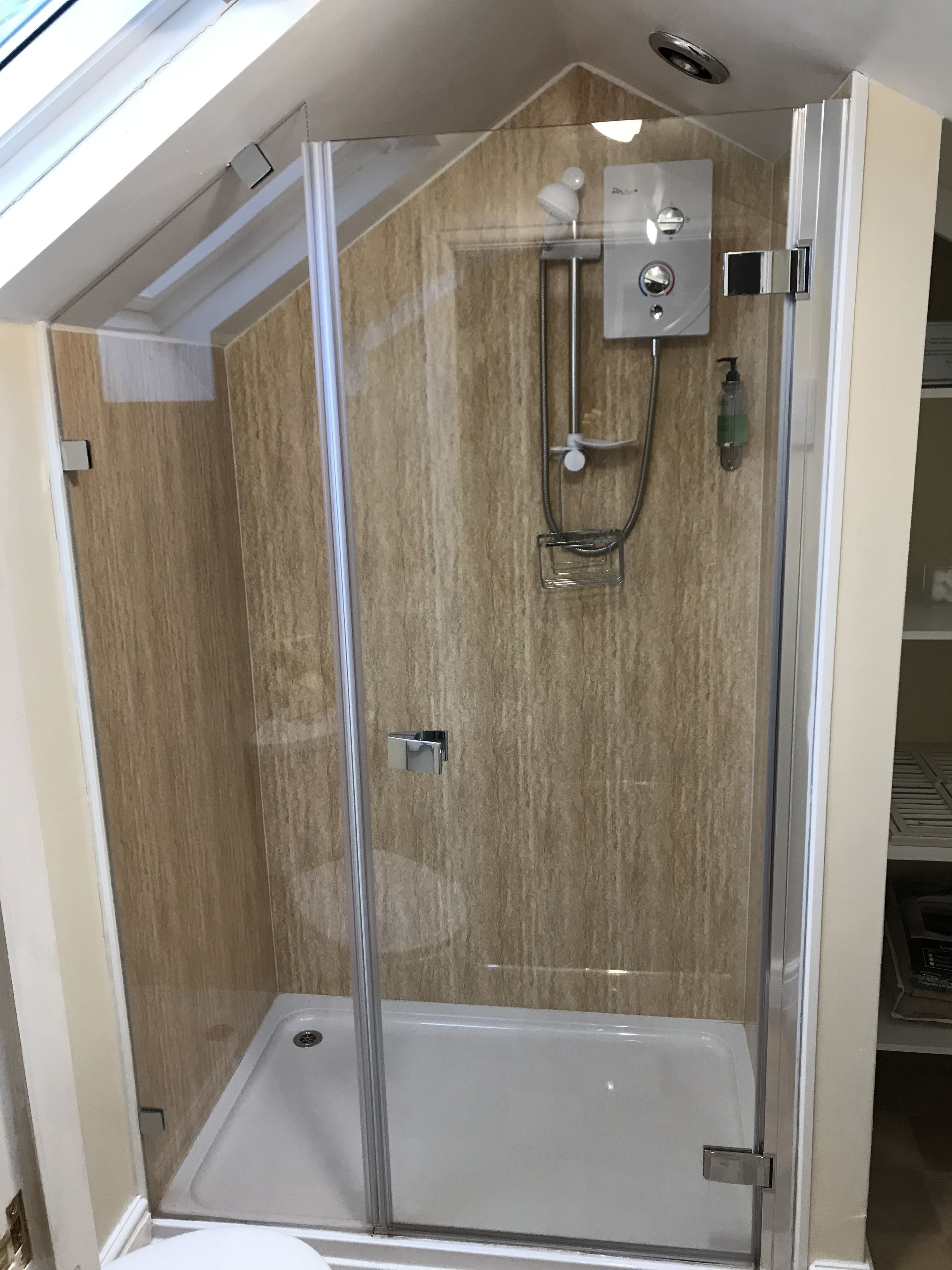 A glass-enclosed shower with a control panel, a handheld showerhead, and a handheld massage nozzle.