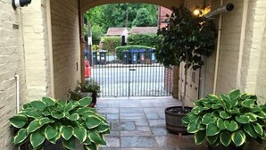 A stone-paved entrance with two large potted plants and a metal gate leading to a street.