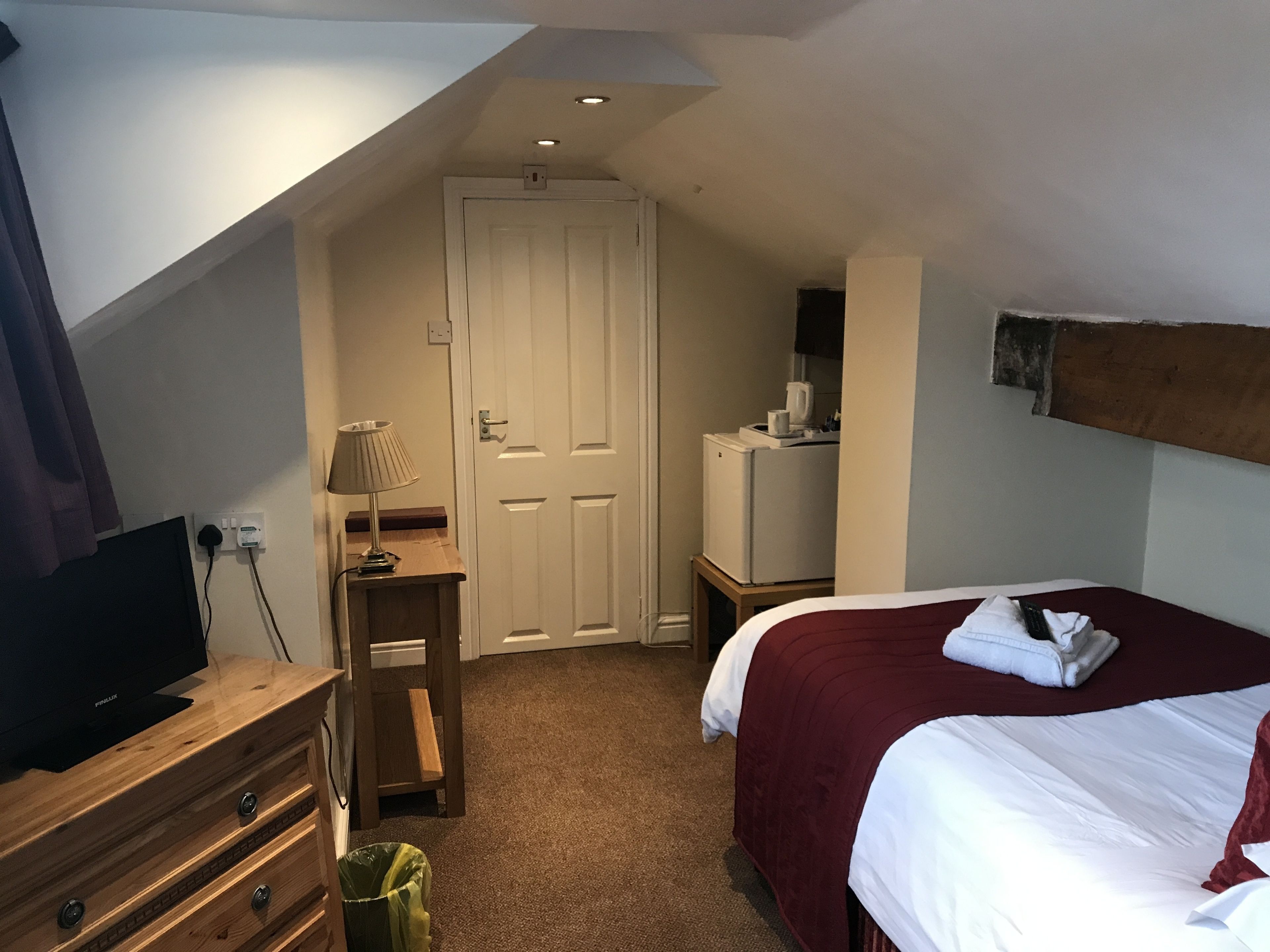 Una habitación de hotel con una cama, un escritorio con lámpara, televisor y refrigerador.