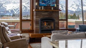Un salon doté d’une cheminée, de canapés en cuir, d’une table basse et offrant une vue sur des montagnes enneigées.