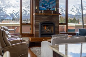 Una sala de estar con chimenea, sofás de cuero, una mesa de centro y vistas a montañas nevadas.