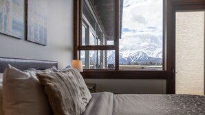 Une chambre à coucher avec un lit, des oreillers, une table de chevet, une lampe et une fenêtre donnant sur la montagne.