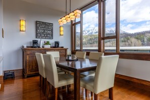 A dining area with a wooden table and chairs, a coffee station, and a view of mountains through large windows.