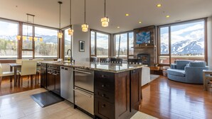 Une cuisine moderne dotée d’un grand îlot central, d’appareils électroménagers en acier inoxydable et de luminaires suspendus.