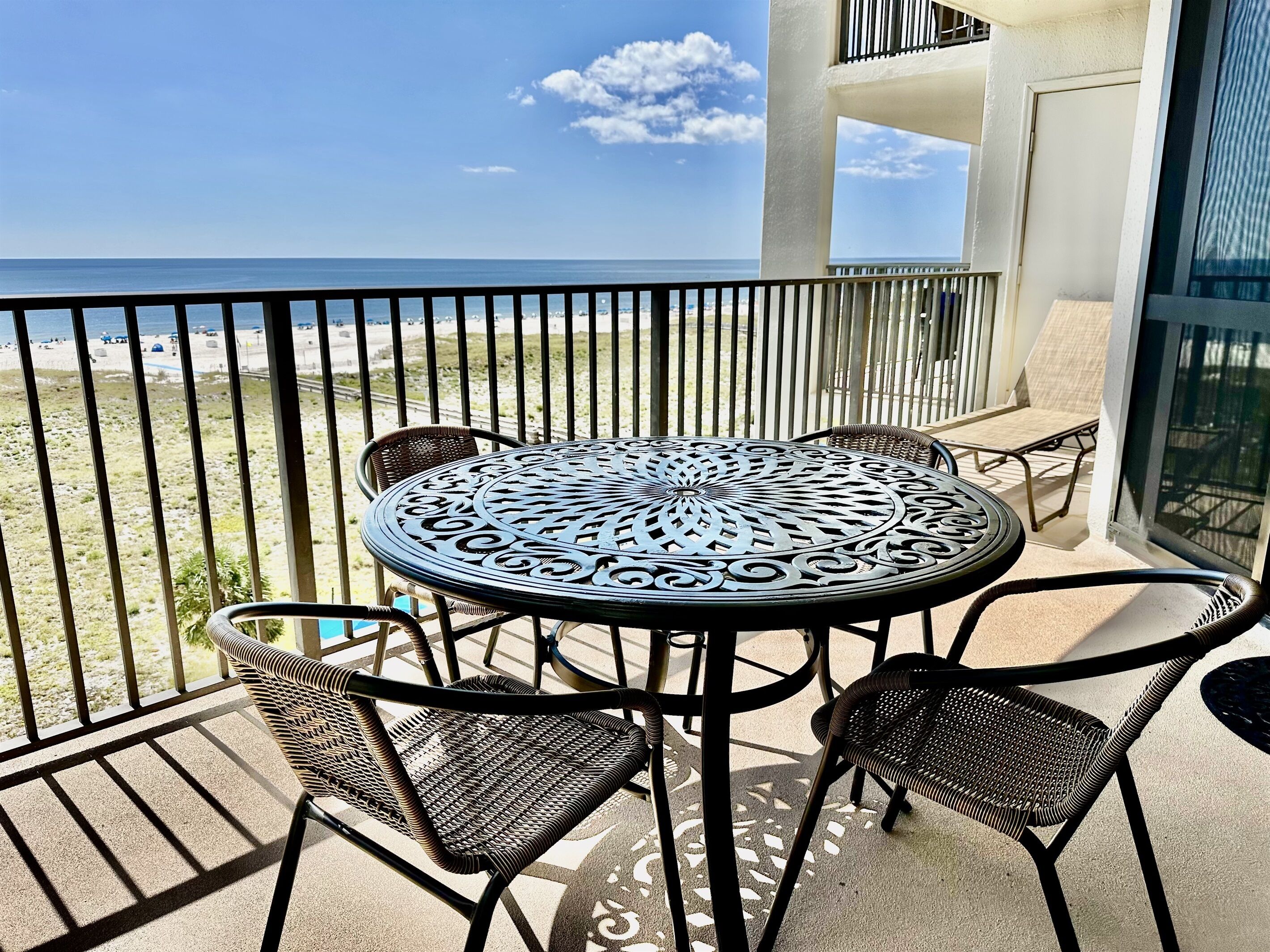 Un balcon avec une table ronde et quatre chaises, donnant sur une plage.