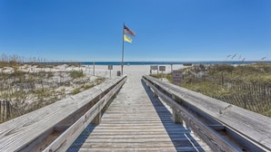 A wooden boardwalk leading to a beach with a caution sign advising to wear protective footwear. - Newly Renovated kitchen in this 2BR Beachfront Condo on the 6th Floor! (Orange Beach)
