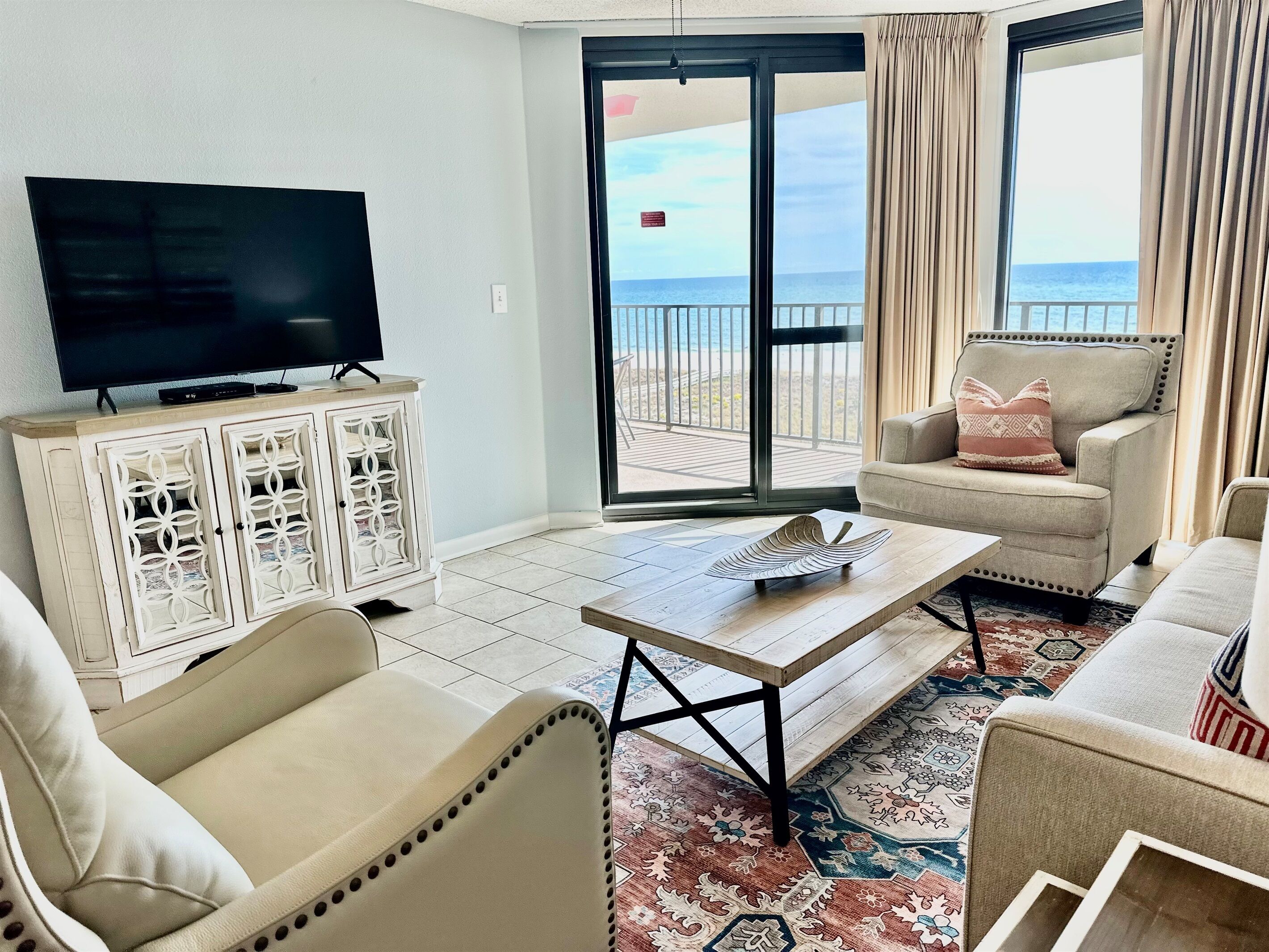 A living room with a television, a sofa, a chair, and a view of the ocean through large sliding doors.