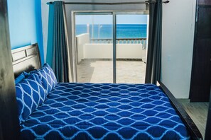 Quarto com cama, vista para o mar através de uma porta de correr e varanda.