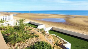 Ein Strandgrundstück mit freiem Blick auf den Ozean, einem Sandstrand und einer angelegten Gartenanlage mit Palmen und Felsen.