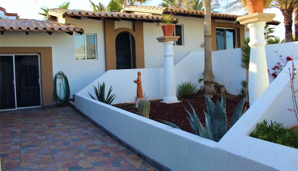 Uma casa com telhado telhado, fachada branca e um jardim com cactos e uma palmeira.