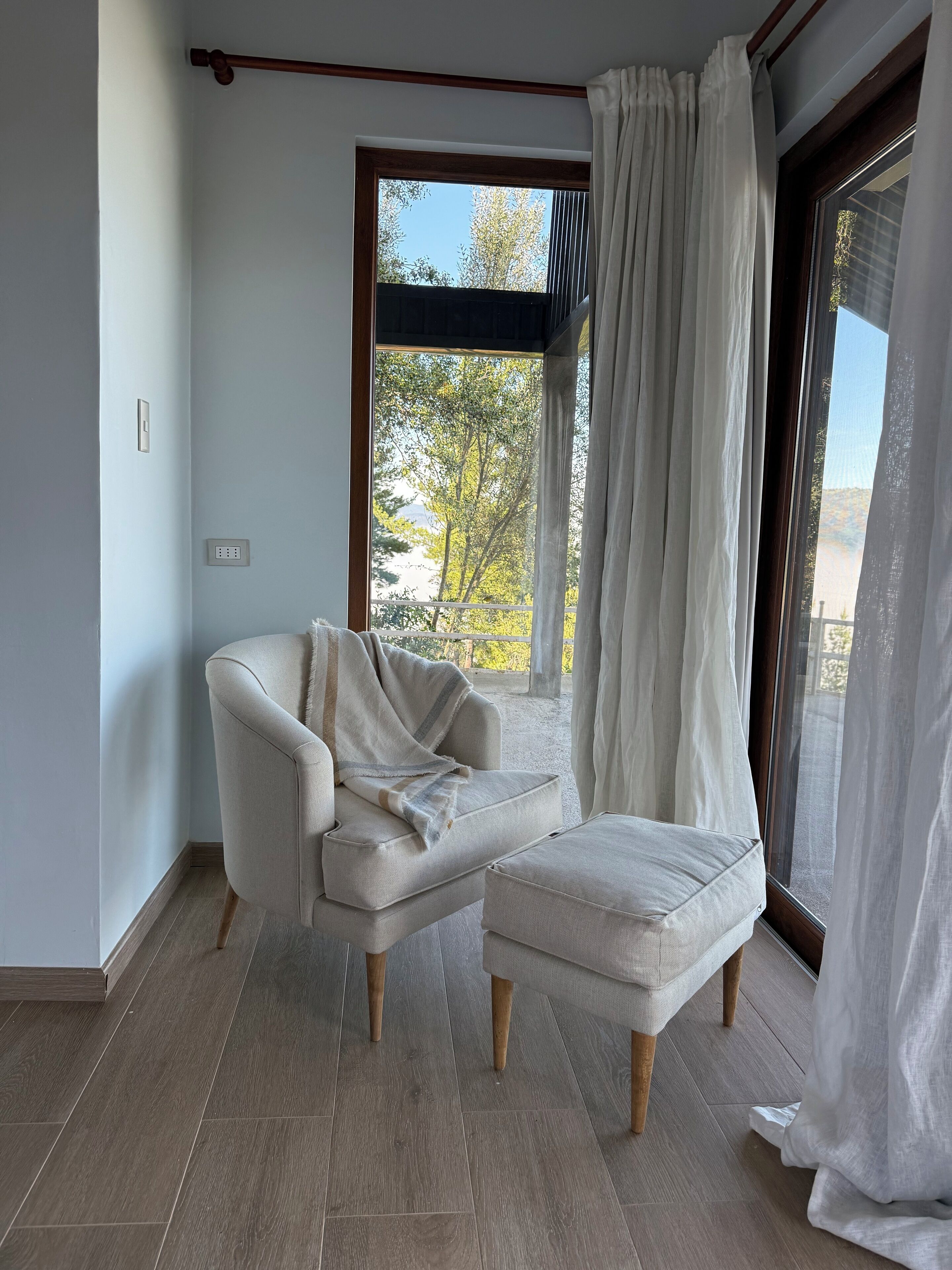 Una habitación moderna con un ventanal grande, un sillón blanco y suelo de madera.