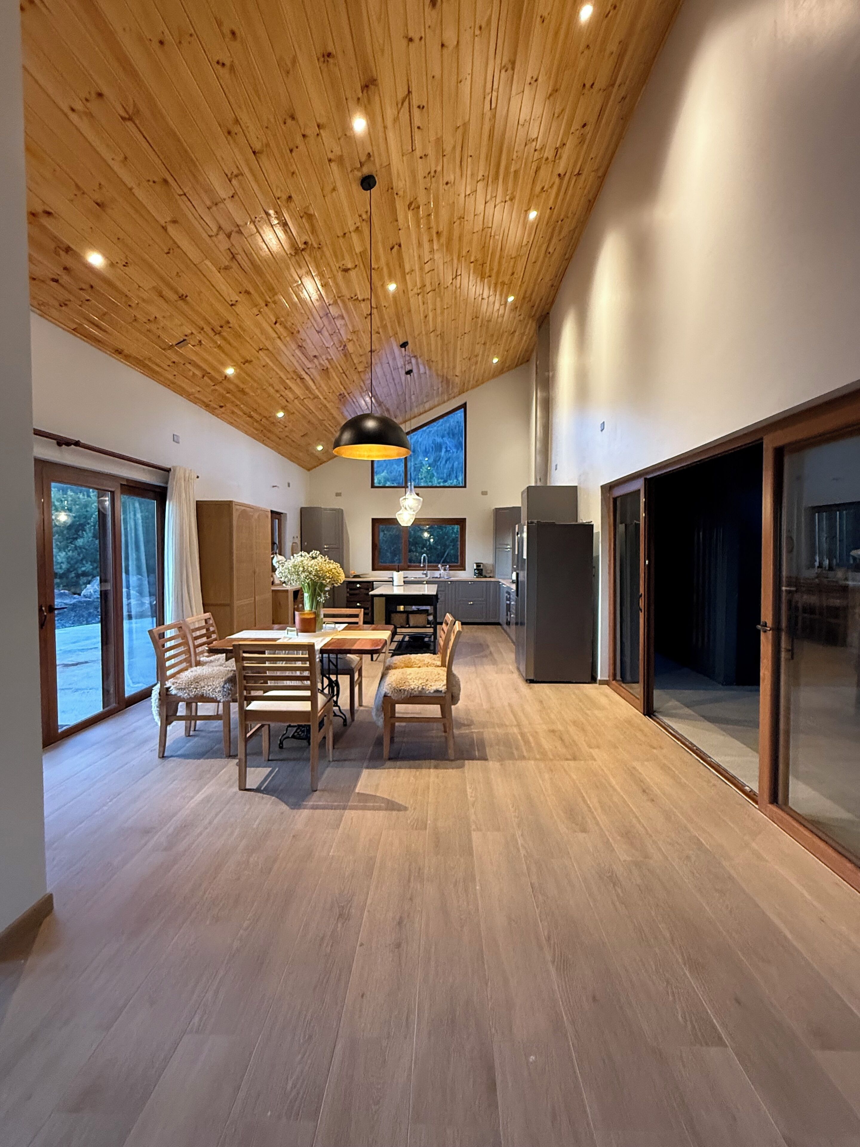 A spacious kitchen with modern appliances, a dining area with wooden furniture, and large windows offering natural light.