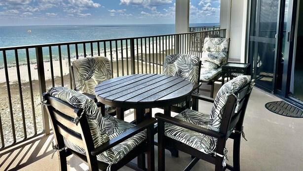 Een balkon met uitzicht op het strand en de oceaan. Er staan vier stoelen en een tafel.