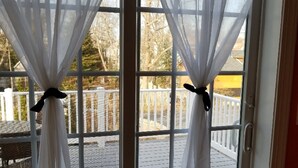 Eine Glasschiebetür mit weißen, zurückgebundenen Vorhängen, die eine Holzterrasse und einen weißen Zaun zeigen.
