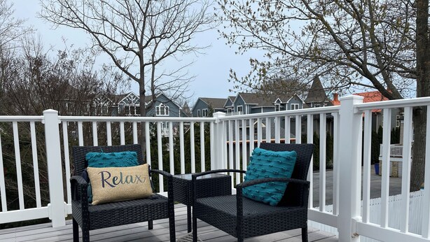 Eine Terrasse mit zwei Korbstühlen, jeweils mit einem türkisblauen Kissen und einem Kissen mit der Aufschrift 'Relax'.
