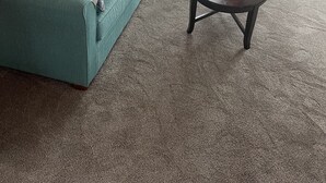 Ein Wohnzimmer mit einem salbeigreenen Sofa und Sessel, einem Glastisch und einer Lampe.