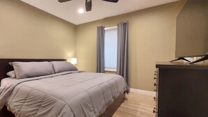 A bedroom with a bed, nightstands, a dresser, a ceiling fan, and a window with curtains. - Recliners. Single Level Living. Walk-in shower. (Rochester)